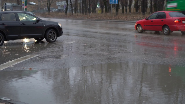 在秋天的雨天，城市交通在潮湿的道路上行驶。路上有个大水坑。视频素材