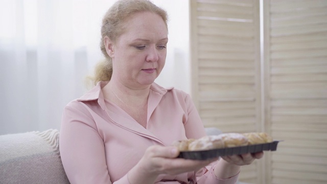 丰满的中年妇女的肖像，闻着美味的新鲜面包。一位白人女士在家里享受新鲜面包的味道。不健康饮食，肥胖观念视频素材