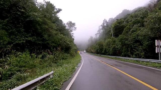 行驶在有黄色标记的柏油路上，穿过雨雾缭绕的热带雨林山脉。视频素材