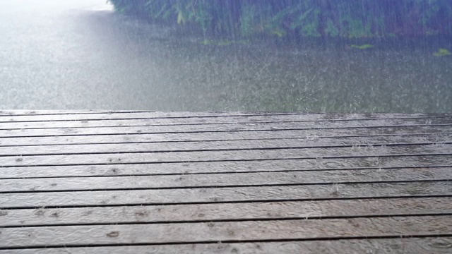 一场大雨敲打着湖面上的木台地，暴雨显示树木被强风吹动。视频素材