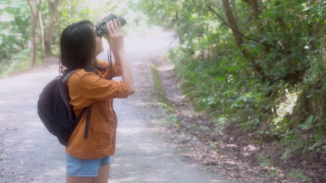 快乐美丽的年轻亚洲女人冒险使用双目在丛林寻找休闲，女孩徒步旅行有背包观光度假在森林露营，假期和夏天的概念。视频素材