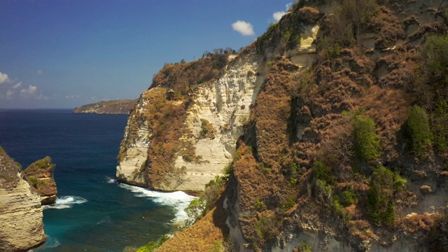 鸟瞰图岩石海岸和海洋与波浪和岩石峭壁努沙佩尼达岛，印度尼西亚巴厘岛。4 k鸟瞰图视频素材