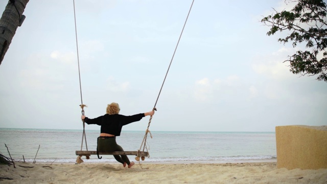 年轻的金发女人在海边的大秋千上荡来荡去。视频素材