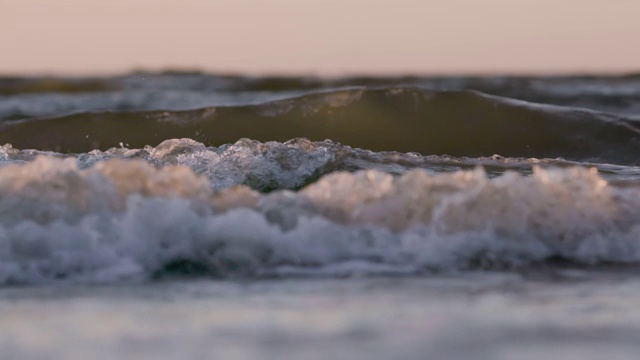 日落时海浪冲向海滩。慢动作海洋白色的水海浪拍击。视频下载