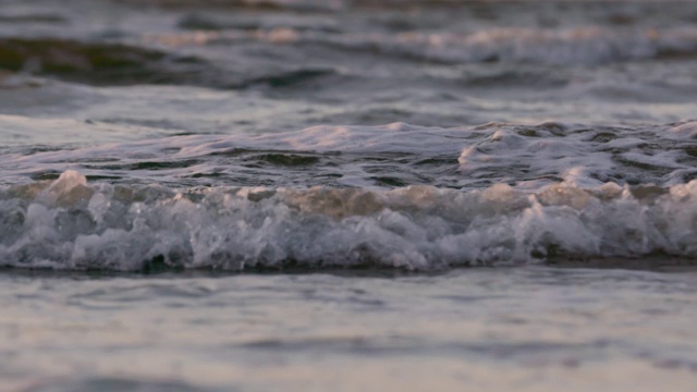 日落时海浪冲向海滩。慢动作海洋白色的水海浪拍击。视频素材