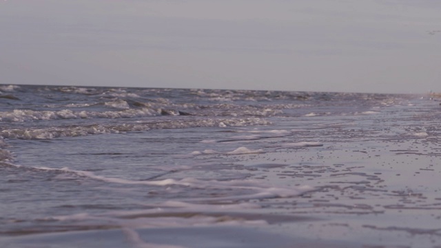 日落时海浪冲向海滩。慢动作海洋白色的水海浪拍击。视频下载