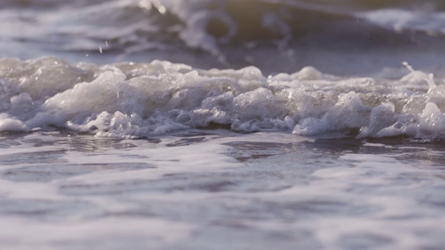 日落时海浪冲向海滩。慢动作海洋白色的水海浪拍击。视频素材