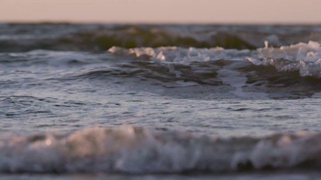 日落时海浪冲向海滩。慢动作海洋白色的水海浪拍击。视频素材