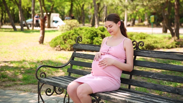 在夏天，孕妇的手在公园的长椅上抚摸肚子的特写视频素材