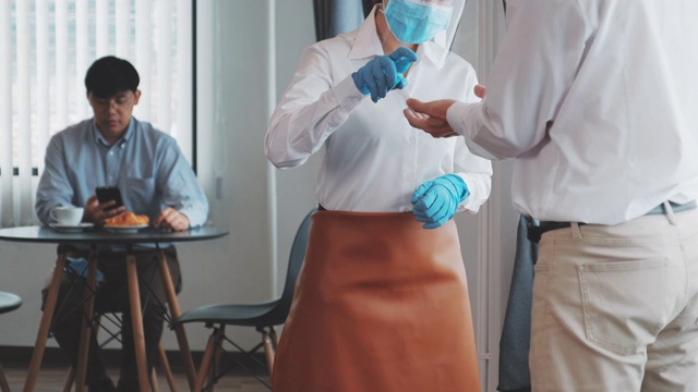 亚洲女招待佩戴防护口罩讲解并使用酒精凝胶清洁洗手扫描顾客体温进入餐厅前，以防止感染冠状病毒，保持社交距离的概念视频素材