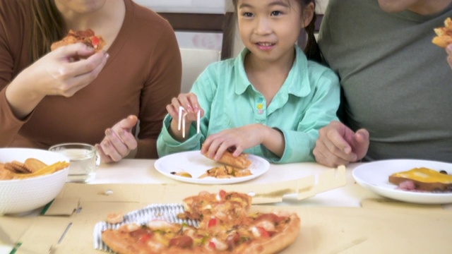 快乐的亚洲母亲和父亲与女儿吃比萨饼在桌子上。视频素材