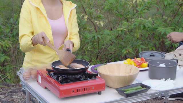 快乐与亚洲女人野餐与烹饪食物放松在夏天，女孩享受和有趣的露营旅程冒险和早餐休闲在假期，背包旅行在营地在假期。视频素材