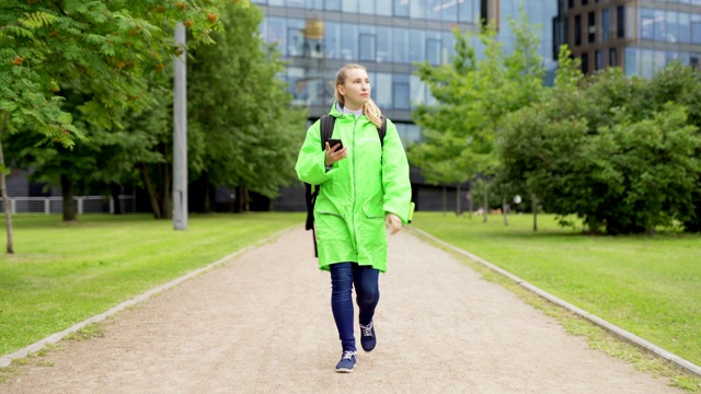 这是一名身穿绿色制服、带着保暖袋的十几岁女食品快递员的全身正面照片，她使用智能手机上的gps应用程序，在送货时四处查看视频素材