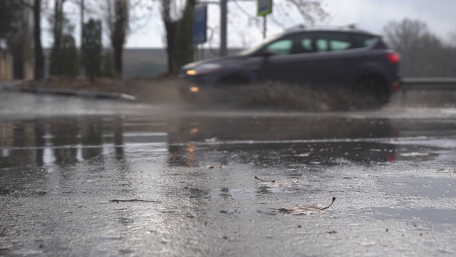 秋天的雨天，城市交通在潮湿的道路上行驶，汽车驶过一个车轮溅起水花的水坑。视频素材