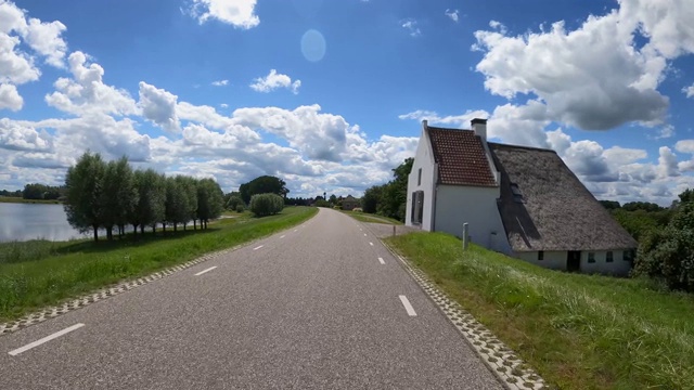 沿着IJssel河行驶，沿途有圩田景观、骑自行车的人和美丽的云彩视频素材