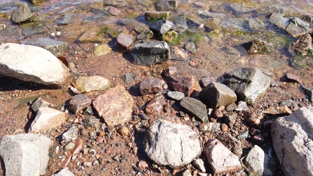 透明水中的石头。海浪逼近多岩石的海岸。涟漪水面视频素材