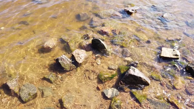 透明水中的石头。海浪逼近多岩石的海岸。涟漪水面视频素材