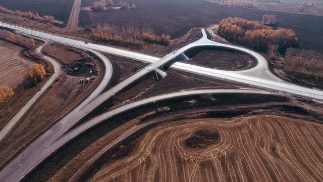 传输连接。道路交汇处正在兴建中。卡车和汽车在公路上行驶。在一个阳光明媚的日子里。运输物流。田野里交通十字路口的鸟瞰图。美丽的秋天字段视频素材