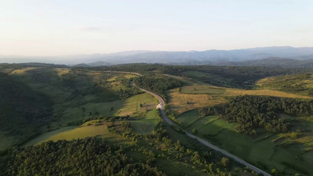 鸟瞰图从上面在绿色的草地和树木之间的山脉的乡村道路周围-自然旅行概念无人机视频在特里西巴在欧洲塞尔维亚在阳光明媚的夏天白天或晚上视频素材