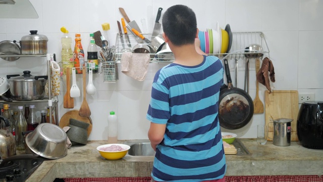 一个十几岁的亚洲男孩帮助他的母亲在切菜板上切鸡肉，为家人准备食物。视频素材