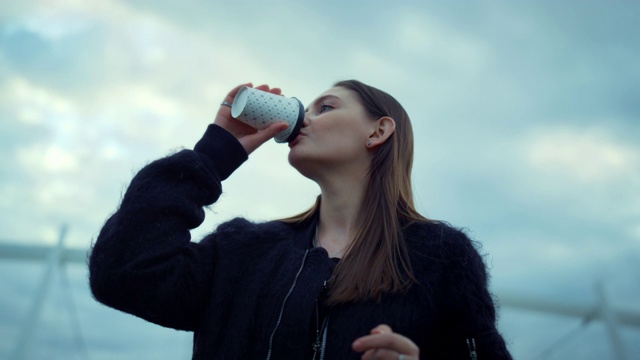 在街上喝外卖咖啡的女孩。女人看手表看时间视频素材