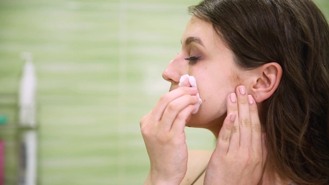 女孩在一个绿色的浴室里用化妆棉卸妆视频素材