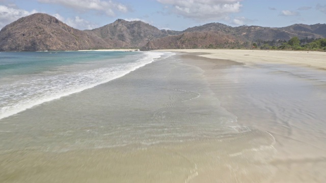 无人机盘旋在海滩海岸，海浪和山和天空的一瞥视频素材