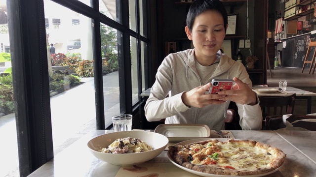 一名女博主用智能手机拍摄美食，在意大利餐厅拍视频，然后在网上发布社交媒体生活方式视频素材