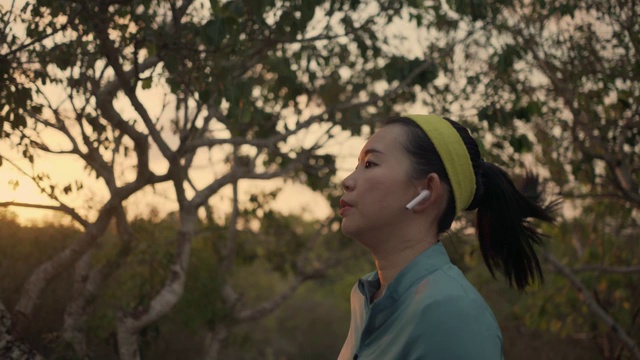 跟踪云台拍摄的年轻和健康的亚洲韩国妇女在户外的树林在日落做慢跑锻炼在美丽的乡村道路视频下载