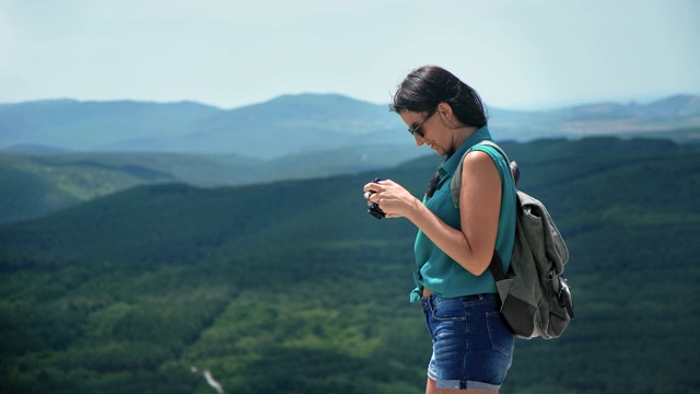 潮女旅行站在山顶用相机拍照。用RED摄像机拍摄4K视频素材