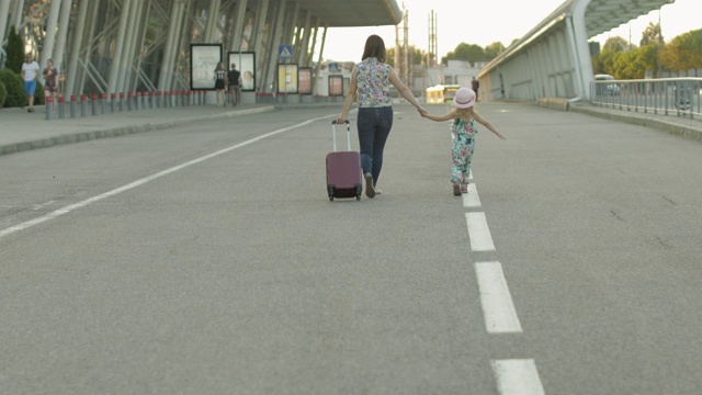 母亲和女儿步行去机场。拎着旅行袋的女人。孩子和妈妈的假期视频素材