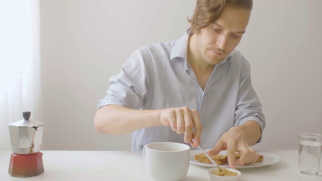 金发白种人早餐端咖啡，在吐司上涂花生酱视频素材