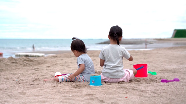 一个小女孩和她的小妹妹在沙滩上玩沙子视频素材