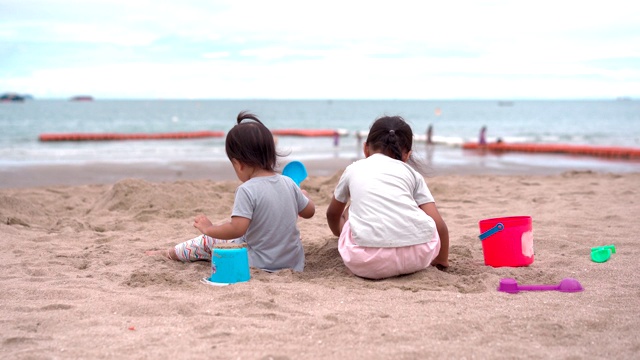 一个小女孩和她的小妹妹在沙滩上玩沙子视频素材