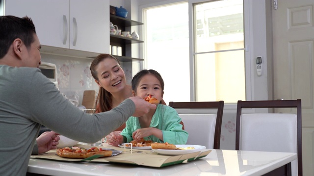 快乐的亚洲母亲和父亲与女儿吃比萨饼在桌子上。视频素材