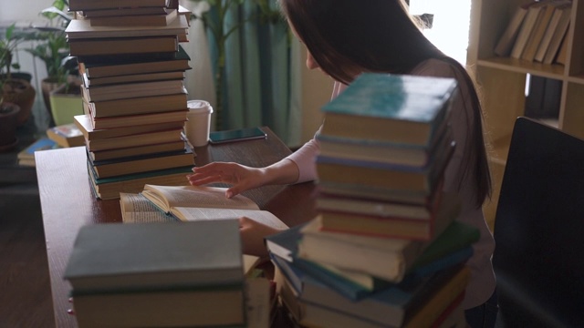 女孩正坐在大学图书馆的桌子旁看书。年轻女子在阅读时翻着纸书。女人学习。回家学习。远程教育。聪明的聪明的女人。视频素材