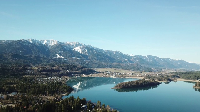 奥地利Faaker See上空的一架无人机。周围有高山山脉，反射在清澈平静的湖面上。小村庄围绕着湖。白雪皑皑的山脉视频素材