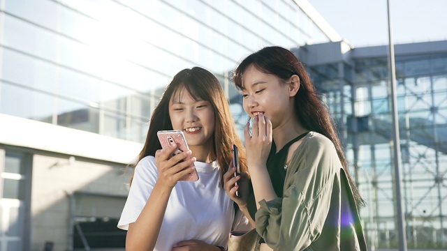 近距离观看快乐可爱的年轻亚洲女孩在时尚服装站在机场前，看着手机视频素材