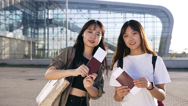 可爱的25岁亚洲女孩，黑色的长发，拿着她们的旅行文件，看着镜头，在机场背景上的美丽微笑视频素材