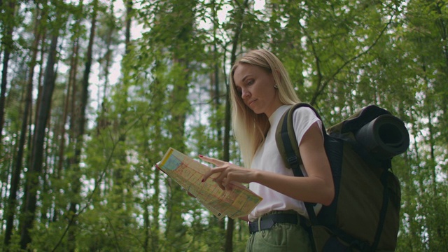 年轻的白人女子在森林徒步旅行时在地图上寻找方向。快乐的女孩在大自然中徒步旅行和在地图的帮助下定向视频素材