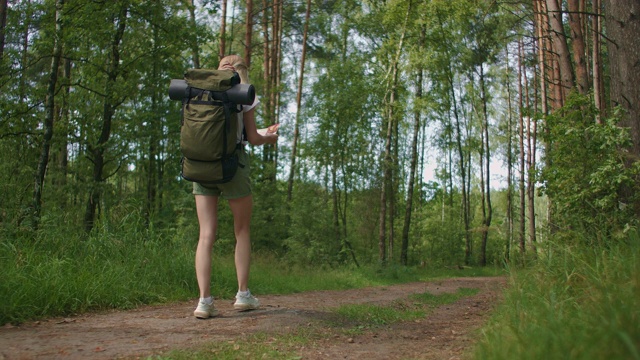 慢镜头后视图:年轻的白人妇女在森林徒步旅行时在地图上寻找方向。快乐的女孩在大自然中徒步旅行和在地图的帮助下定向视频素材