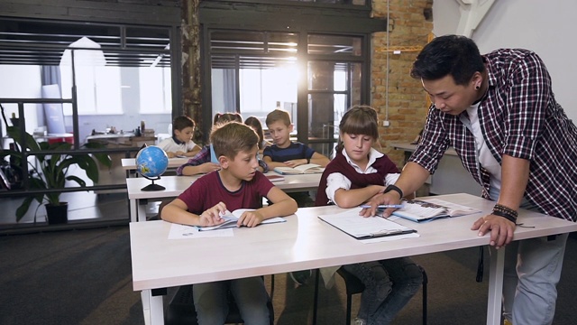 一组小学白人学生在课堂上独立学习，而韩国男老师在讲解并帮助两名学生视频素材