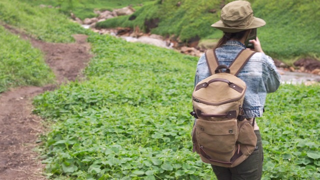 年轻的亚洲女性旅行者背包在山间徒步旅行，用智能手机相机拍下小溪和美丽的自然在暑假。旅行和户外活动的概念。视频素材