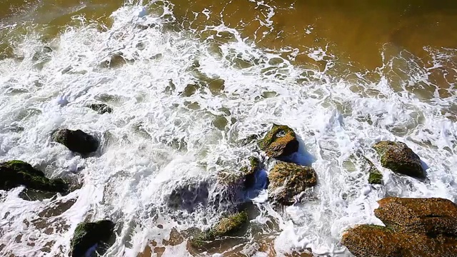 海浪和冲浪白色泡沫的海滩或海洋与岩石在晴朗的日子。视频素材