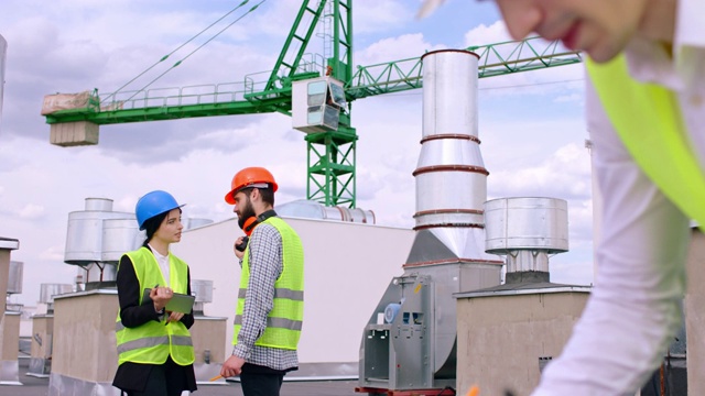 在建筑顶部的大型建筑工地上，女士和戴着安全帽的工程师们讨论着一些事情，另一个商人写了一些关于建筑计划的注释视频素材