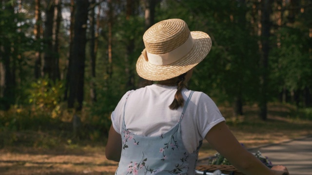 快乐美丽的女人与自行车户外。日落时分，身着蓝色夏装的迷人女孩在公园里骑着复古自行车。复古风格，年轻女性骑着复古自行车穿越绿色森林视频素材