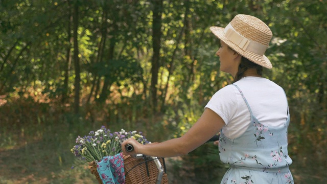 年轻浪漫美丽的旅行者女人在帽子和夏装与复古自行车在日落森林。迷人的女孩骑着自行车，手里拿着花篮。夏日公园假期快乐视频素材