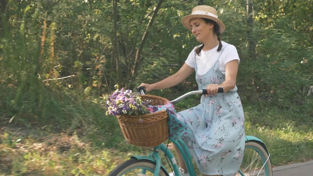 在夏日阳光明媚的绿色公园里，浪漫迷人的骑自行车的女人骑着一辆老式自行车。迷人的女性在复古自行车上移动。快乐的微笑女孩是放松的自行车在假期视频素材