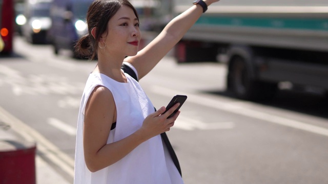 年轻的亚洲女子在城市为她的车叫手机在她的手视频素材