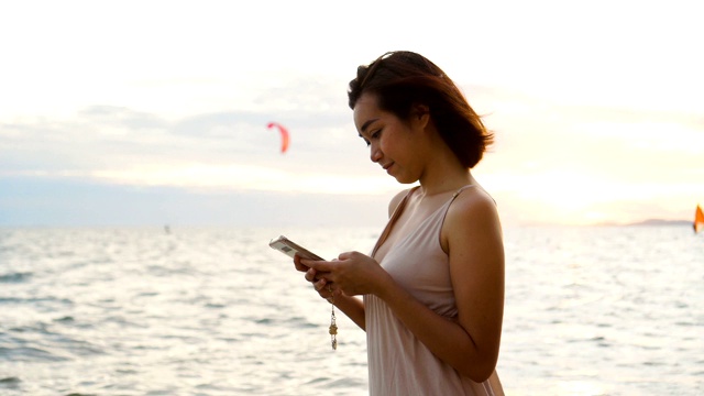 沙滩上的女人在日落海滩上使用社交媒体。视频素材